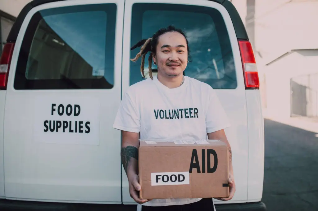 A volunteer holding a box of food aid in front of a supply vehicle, symbolizing generosity and help.