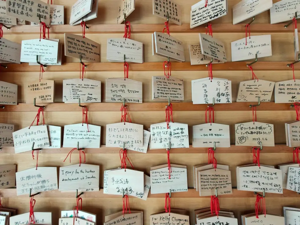 A close-up view of wooden prayer plaques with handwritten wishes in a temple setting.