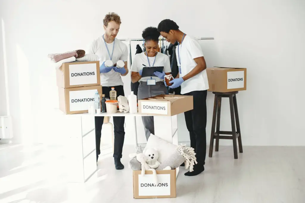 Three volunteers organize donation boxes filled with essentials in a bright indoor setting.