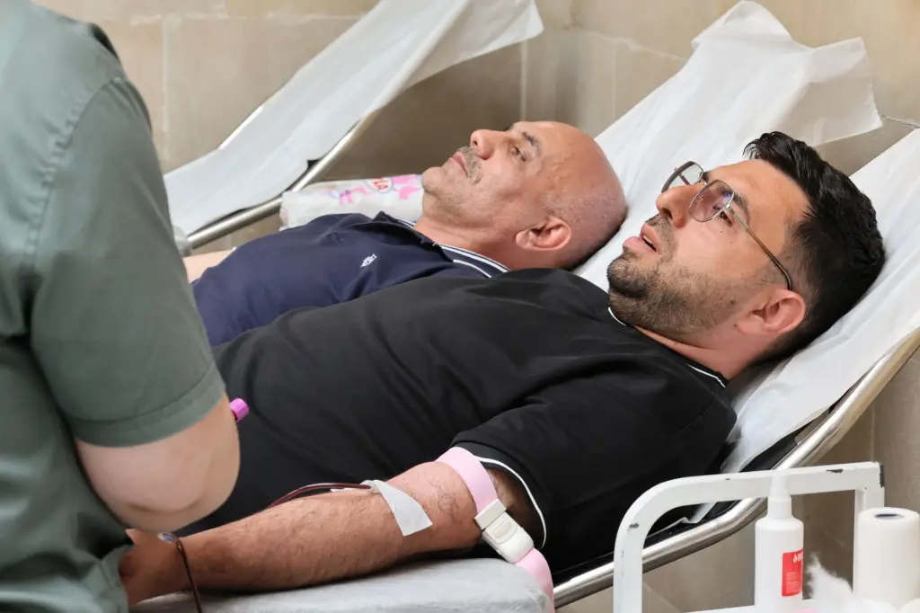 Two men are lying on medical beds while donating blood at a clinic.