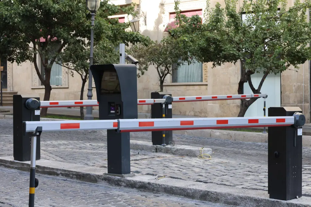 Modern parking barrier gate system on cobblestone street with greenery.