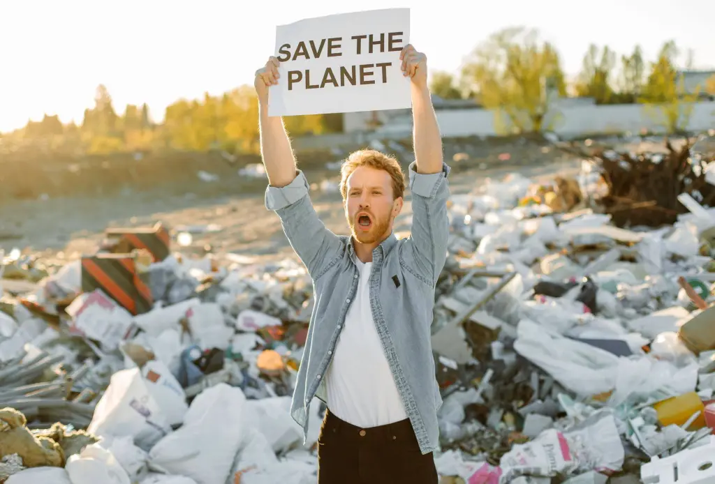 Passionate activist holding sign to save the planet at a landfill, promoting environmental awareness.