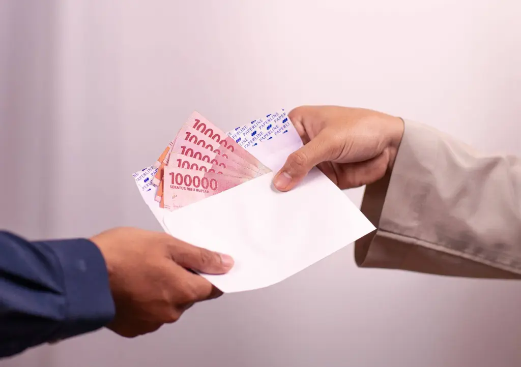 Hands giving and receiving Indonesian rupiah in an envelope, symbolizing financial transaction.