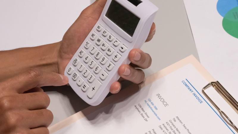 Close-up of hands using a calculator next to a company invoice, depicting a financial calculation concept.